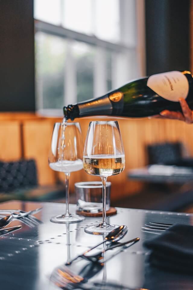 Black woman pouring a glass of wine at a restaurant | How to pair caviar and wine | Bon Vie magazine